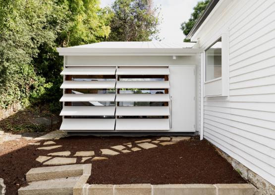 a white shed with a white wall and brown dirt around it