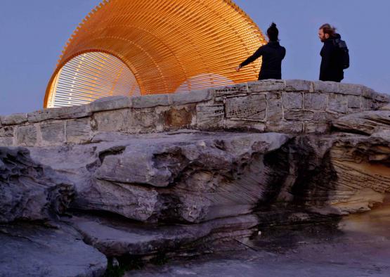 a couple of people standing on a rock ledge looking at a large round object