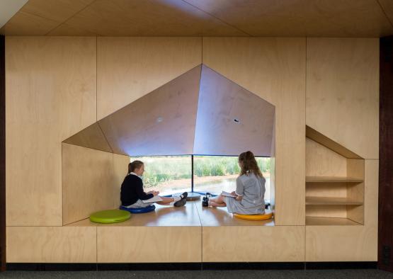 two girls sitting on a bench in a room with a triangular window